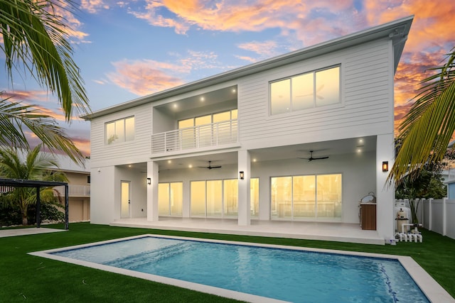 back house at dusk featuring ceiling fan, a balcony, a yard, and a patio area