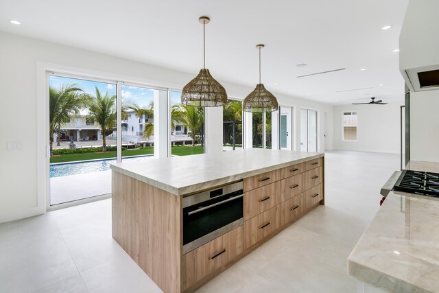 kitchen featuring a large island, stainless steel appliances, light stone counters, light brown cabinetry, and decorative light fixtures