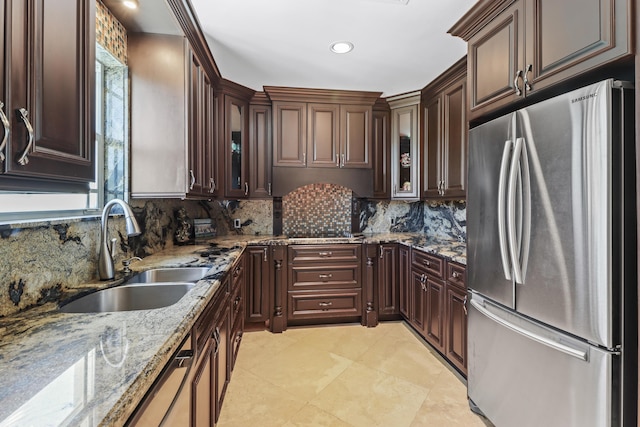 kitchen with a sink, glass insert cabinets, light stone counters, and freestanding refrigerator