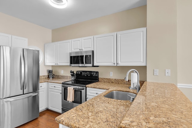 kitchen featuring white cabinetry, sink, stainless steel appliances, light stone countertops, and light wood-type flooring