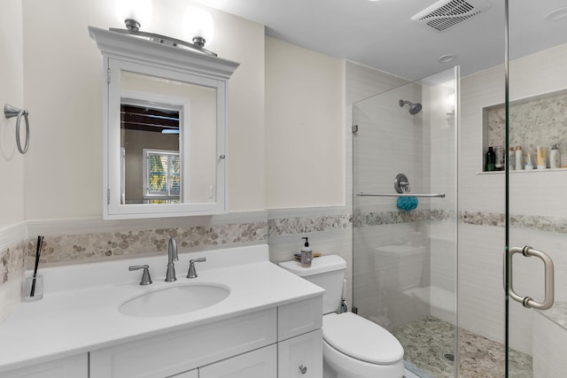 bathroom with toilet, tile walls, vanity, and a shower with shower door