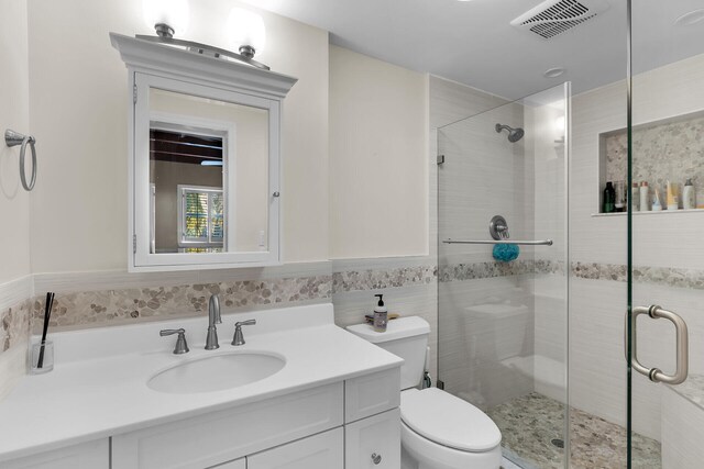 bathroom with toilet, tile walls, vanity, and a shower with shower door