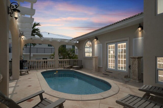 pool at dusk with a patio area and french doors