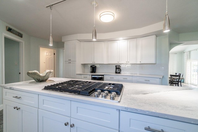 kitchen with white cabinetry, stainless steel gas stovetop, decorative light fixtures, and beverage cooler