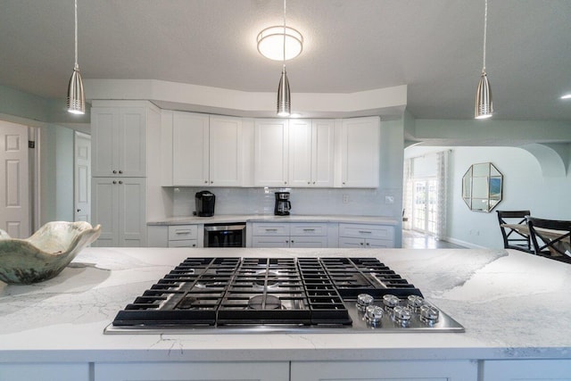 kitchen featuring pendant lighting, stainless steel gas stovetop, white cabinetry, beverage cooler, and light stone countertops