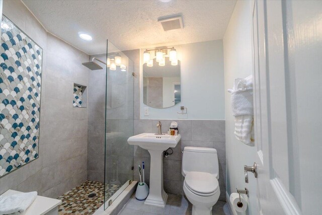 bathroom featuring sink, tile walls, tiled shower, toilet, and a textured ceiling