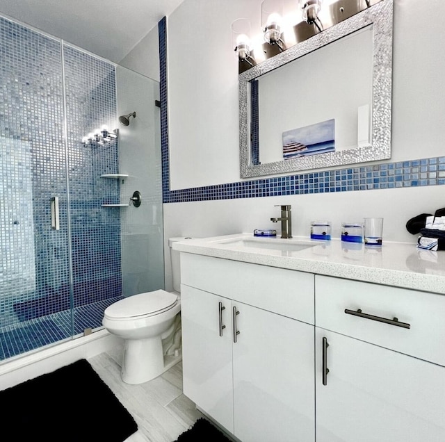 bathroom featuring vanity, backsplash, a shower with door, and toilet