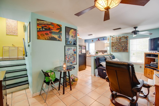 living area featuring light tile patterned floors, ceiling fan, visible vents, and baseboards