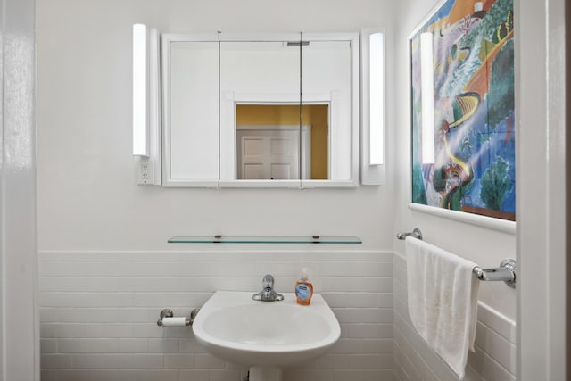 bathroom with wainscoting, a sink, and tile walls