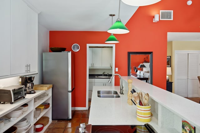 kitchen featuring decorative light fixtures, visible vents, freestanding refrigerator, white cabinetry, and a sink