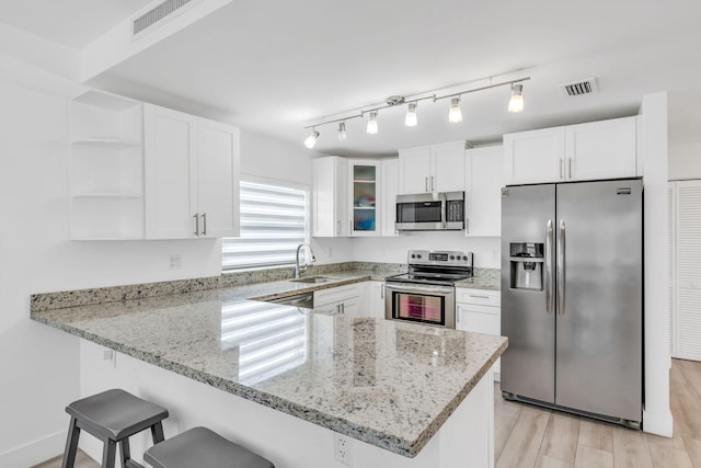 kitchen featuring sink, stainless steel appliances, light stone counters, white cabinets, and kitchen peninsula