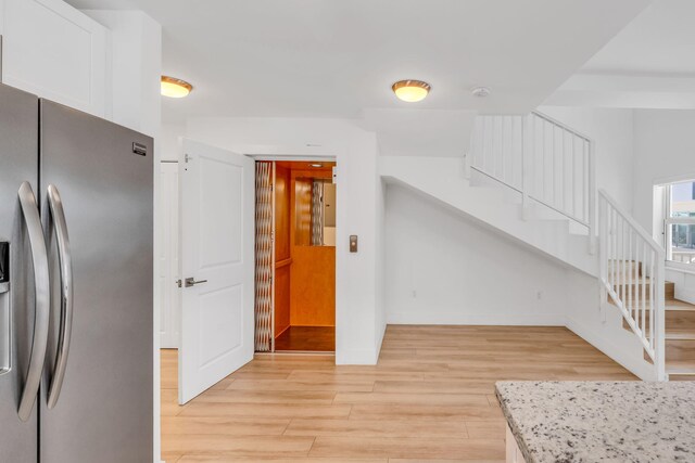 kitchen featuring white cabinetry, stainless steel fridge, light stone counters, and light hardwood / wood-style flooring