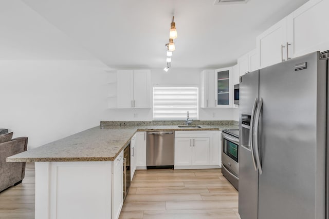 kitchen with sink, appliances with stainless steel finishes, light stone counters, white cabinets, and kitchen peninsula