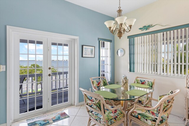 dining space featuring a water view, light tile patterned floors, a notable chandelier, and french doors