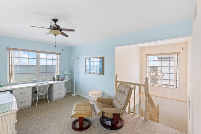 office space with ceiling fan with notable chandelier, plenty of natural light, light colored carpet, and built in desk