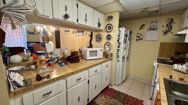 kitchen with a paneled ceiling, white cabinetry, sink, light tile patterned floors, and white appliances