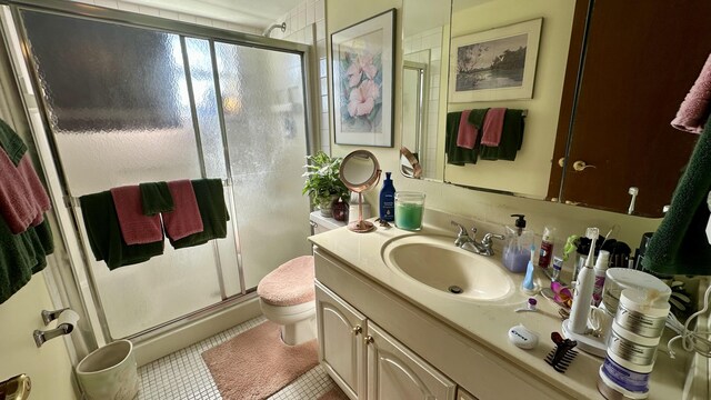 bathroom with a shower with door, vanity, tile patterned flooring, and toilet