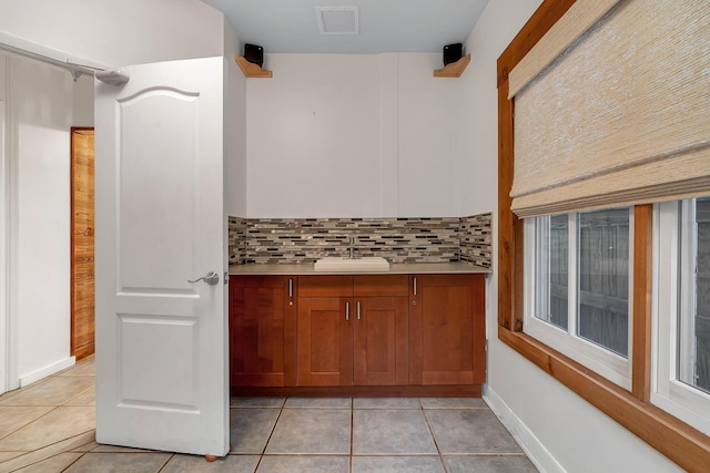 bar featuring tasteful backsplash, light tile patterned flooring, a sink, and visible vents