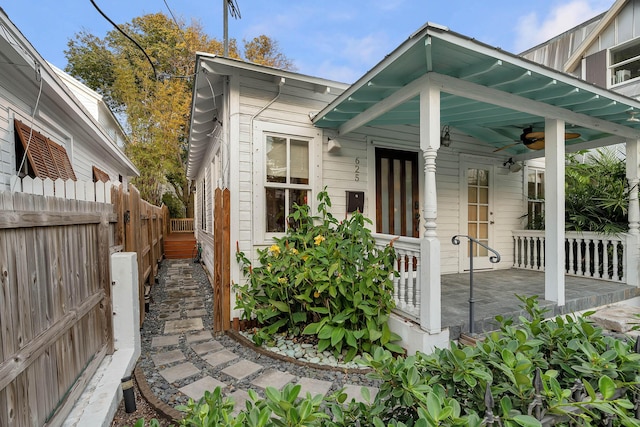 view of side of property with covered porch, ceiling fan, and fence