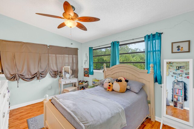 bedroom featuring ceiling fan, lofted ceiling, a textured ceiling, and light hardwood / wood-style floors