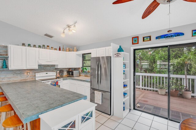 kitchen with lofted ceiling, appliances with stainless steel finishes, white cabinetry, a kitchen breakfast bar, and kitchen peninsula