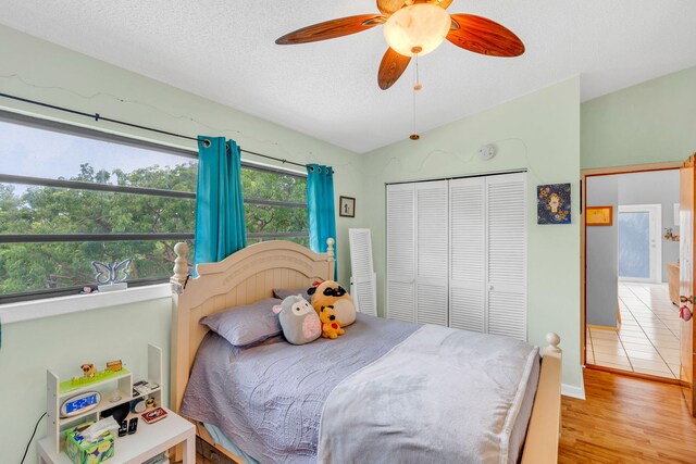 bedroom with vaulted ceiling, light hardwood / wood-style flooring, a textured ceiling, a closet, and ceiling fan