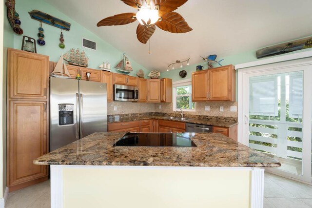 kitchen with a kitchen island, vaulted ceiling, dark stone counters, and appliances with stainless steel finishes