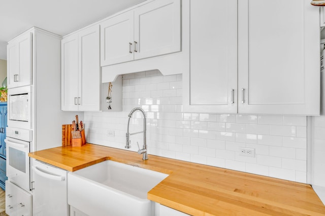 kitchen with white appliances, a sink, butcher block countertops, white cabinets, and tasteful backsplash