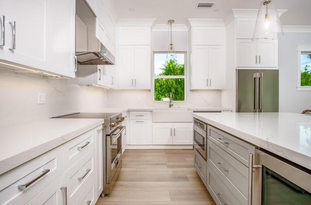 kitchen with white cabinets, wall chimney range hood, decorative light fixtures, and premium appliances