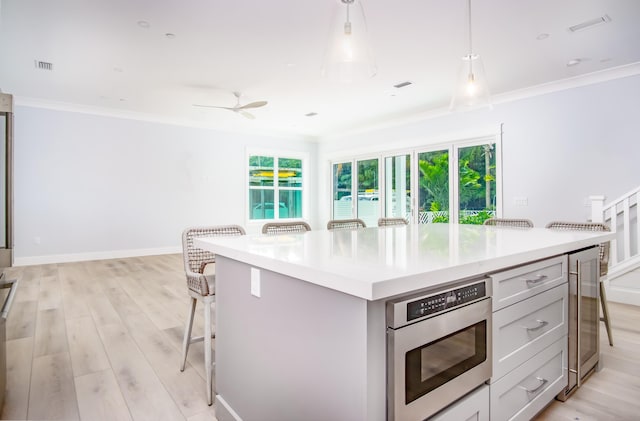 kitchen with pendant lighting, wine cooler, a kitchen breakfast bar, ornamental molding, and a center island