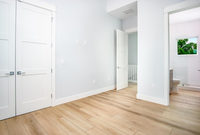 unfurnished bedroom with ensuite bathroom, light wood-type flooring, and a closet