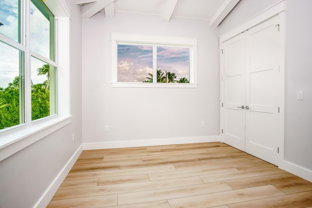 unfurnished bedroom with light wood-type flooring, beam ceiling, and a closet