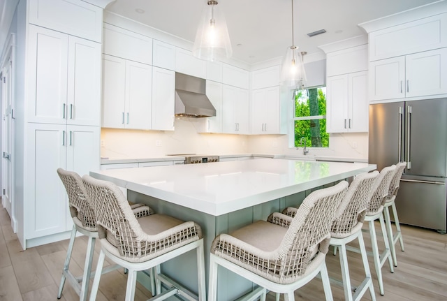 kitchen with a breakfast bar, wall chimney exhaust hood, high end fridge, and a kitchen island