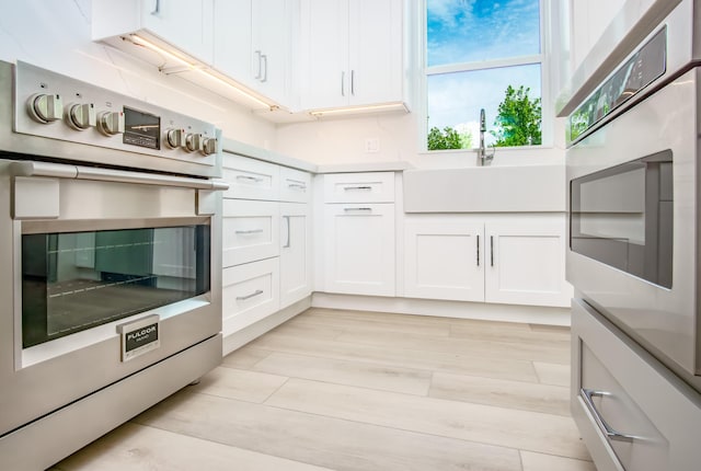 kitchen with oven, light wood-type flooring, and white cabinets