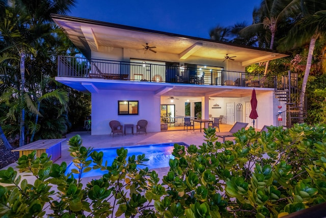 back house at twilight featuring a balcony, a patio, and ceiling fan