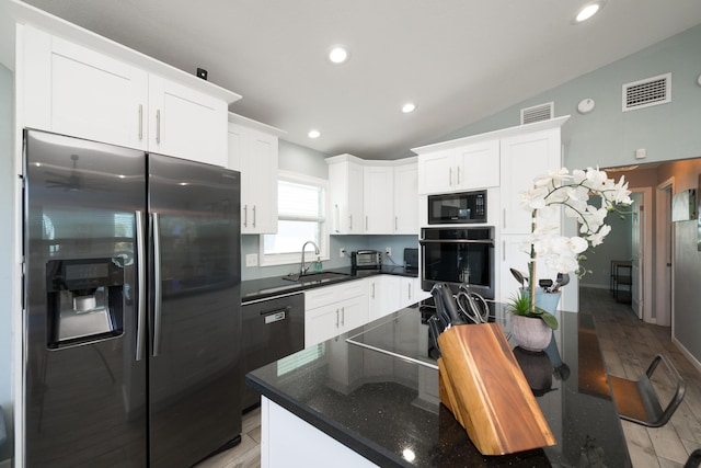 kitchen featuring sink, dark stone countertops, black appliances, white cabinets, and vaulted ceiling