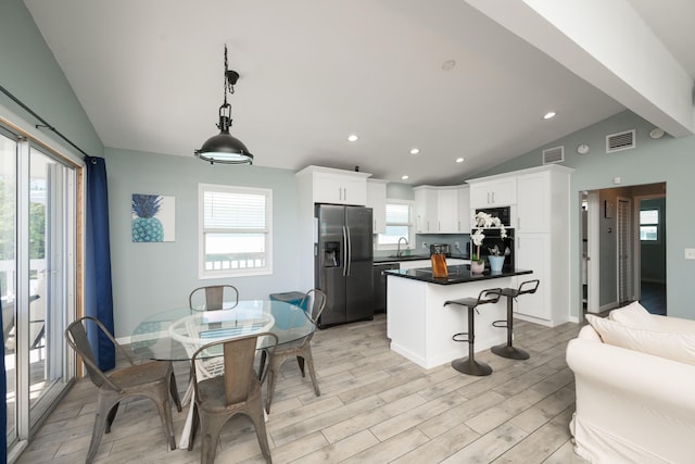 kitchen featuring lofted ceiling, sink, stainless steel refrigerator with ice dispenser, white cabinets, and decorative light fixtures