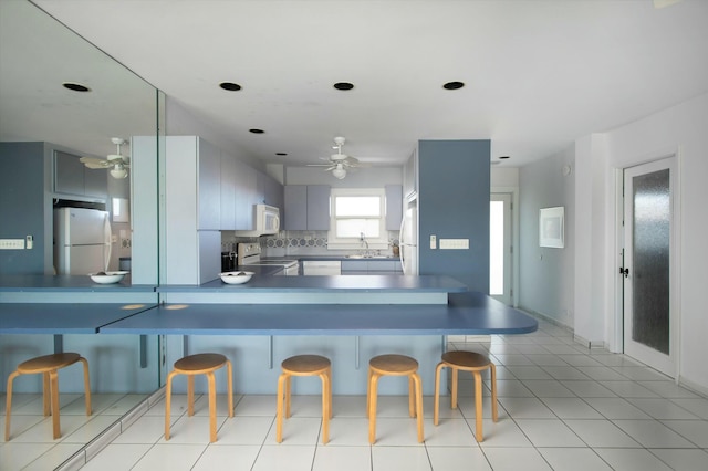 kitchen featuring sink, a breakfast bar area, backsplash, kitchen peninsula, and white appliances