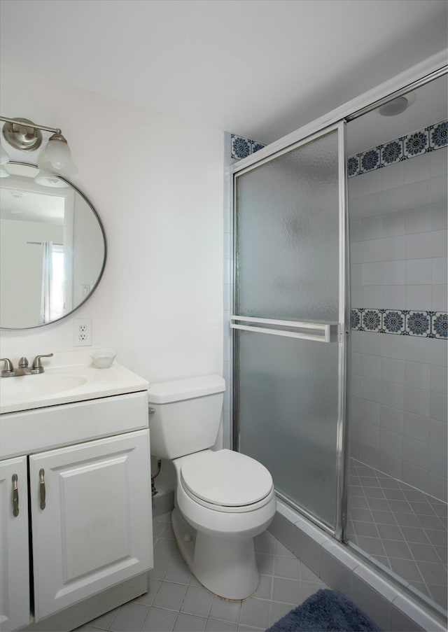 bathroom featuring tile patterned flooring, vanity, a shower with shower door, and toilet