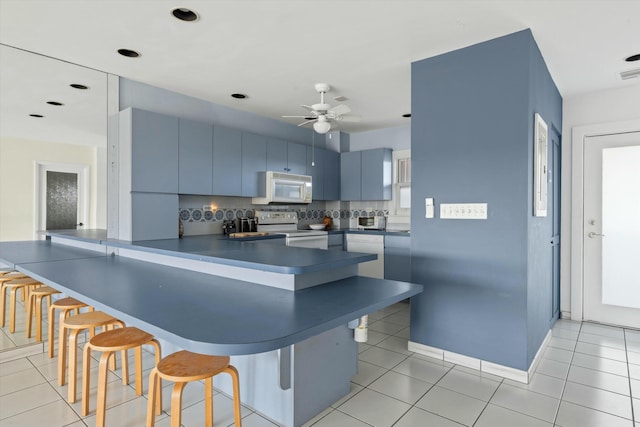 kitchen with blue cabinetry, a kitchen breakfast bar, kitchen peninsula, white appliances, and decorative backsplash