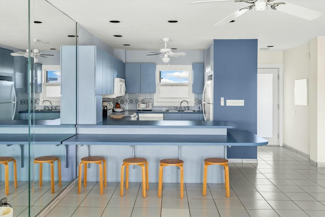 kitchen featuring white appliances, a breakfast bar, blue cabinets, and kitchen peninsula