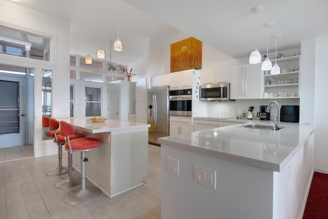 kitchen with appliances with stainless steel finishes, a sink, light wood finished floors, and open shelves