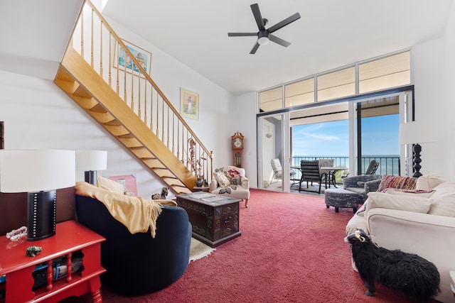 carpeted living room with stairs, a wall of windows, and a ceiling fan