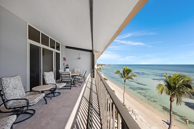 balcony featuring a view of the beach, a sunroom, and a water view