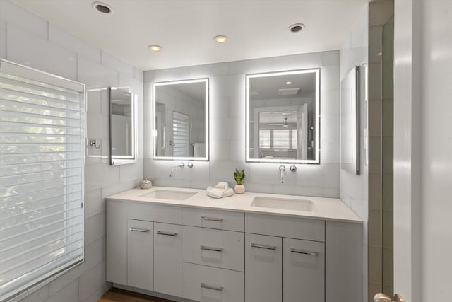 bathroom with double vanity, tile walls, a sink, and recessed lighting