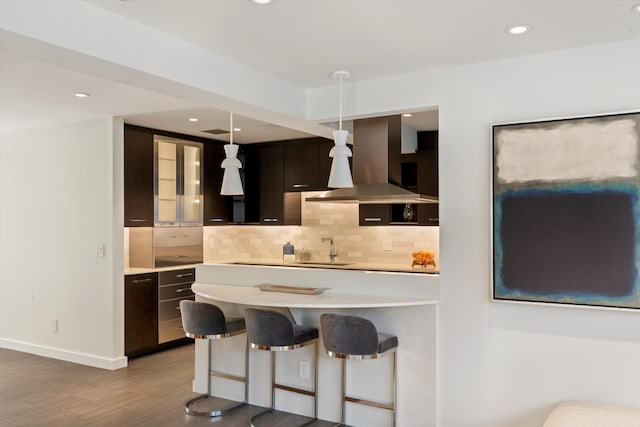 kitchen with a sink, backsplash, wall chimney exhaust hood, and dark brown cabinets