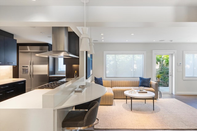 kitchen with wall chimney exhaust hood, appliances with stainless steel finishes, dark cabinets, wood finished floors, and recessed lighting