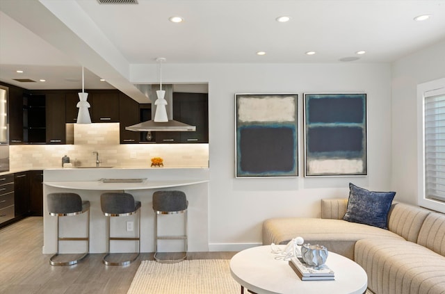 kitchen with recessed lighting, a kitchen breakfast bar, light countertops, decorative backsplash, and light wood finished floors