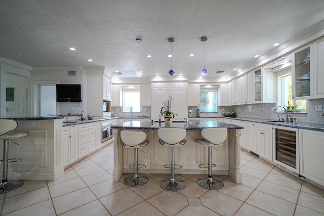 kitchen with hanging light fixtures, white cabinetry, a kitchen island, and beverage cooler