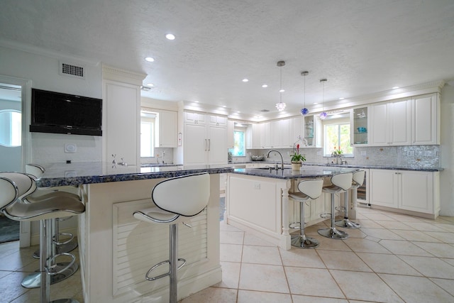 kitchen featuring pendant lighting, white cabinetry, dark stone countertops, a kitchen breakfast bar, and a center island